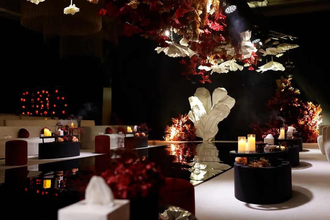 Mirror runway leading to a white petal sculpture, framed by red floral trees and candlelit tables