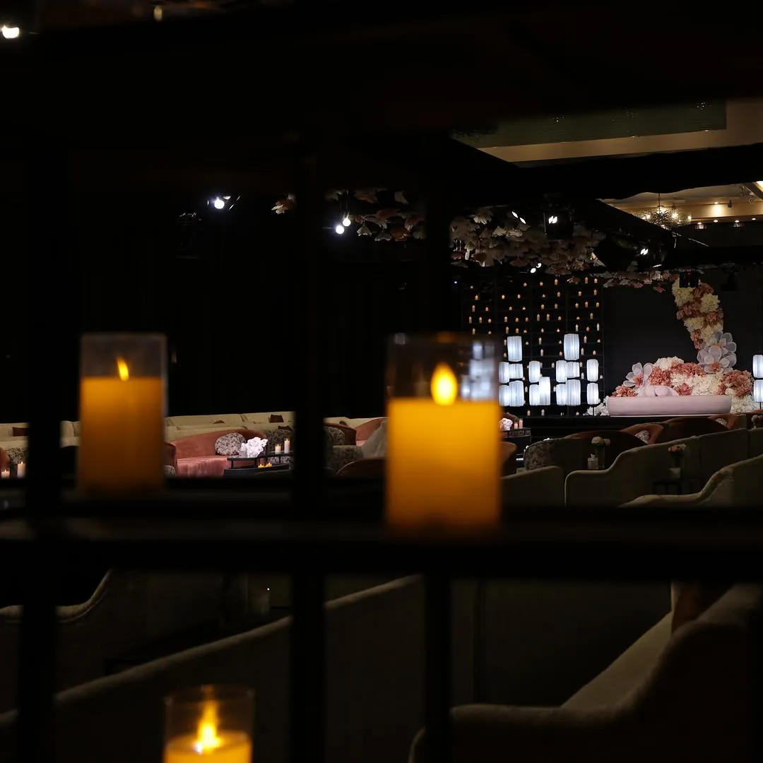 Candles in the foreground framing a hall with a floral stage and ceiling florals