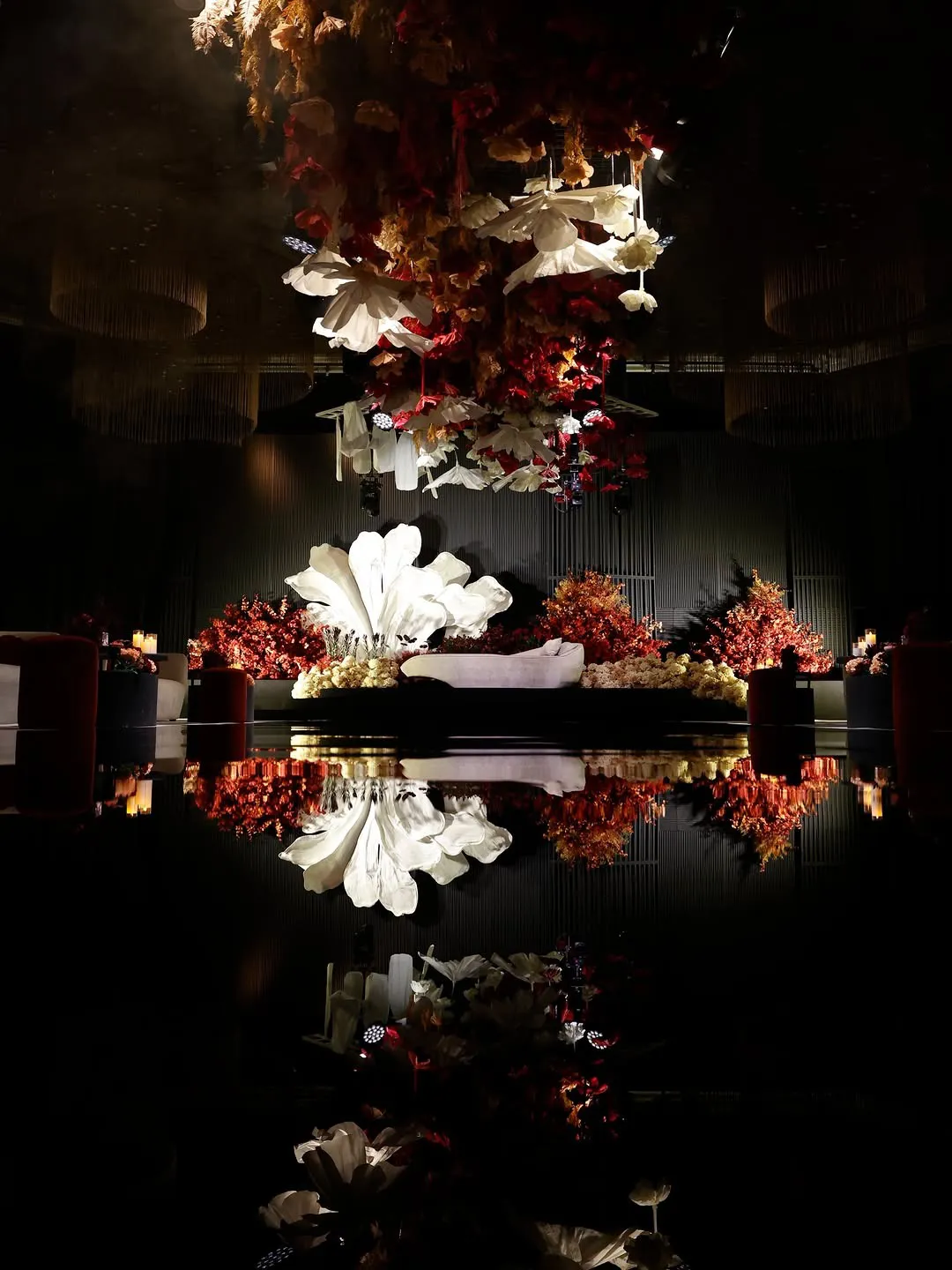 Red and ivory florals suspended above a stage with a white floral statement, mirrored in a black runway