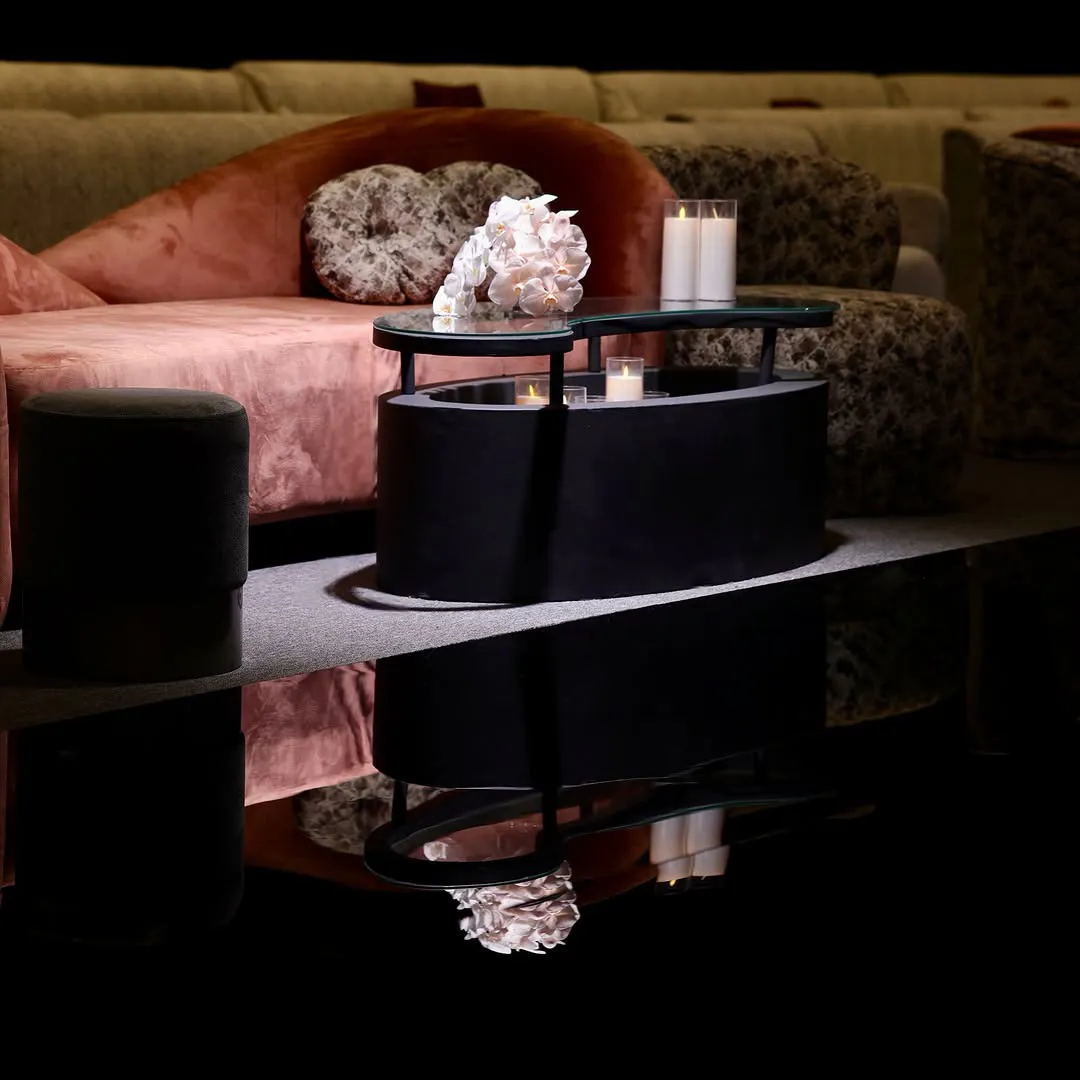 Blush orchids and candles on a black glass-top table beside a rose velvet sofa