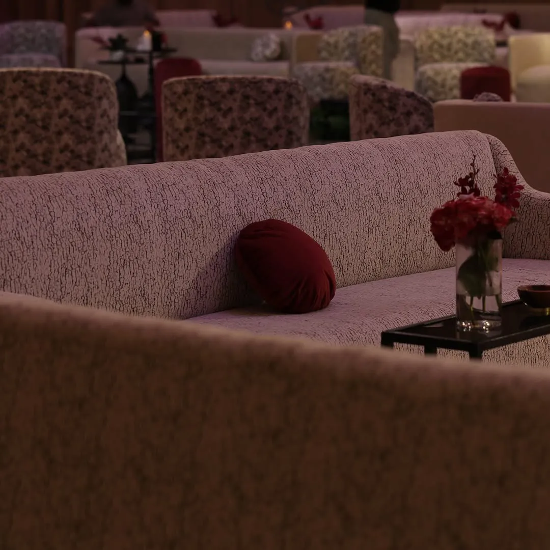 Textured sofa with a red velvet cushion and red blooms in a glass vase on a side table